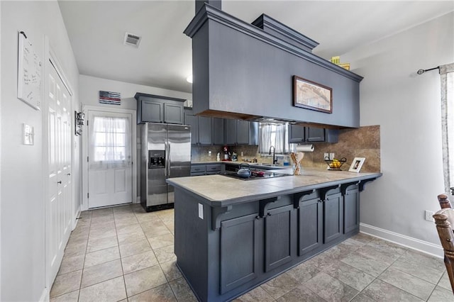 kitchen featuring backsplash, stainless steel fridge with ice dispenser, light countertops, a peninsula, and a sink