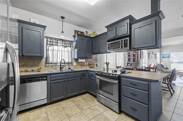 kitchen featuring pendant lighting, decorative backsplash, a peninsula, stainless steel appliances, and a sink