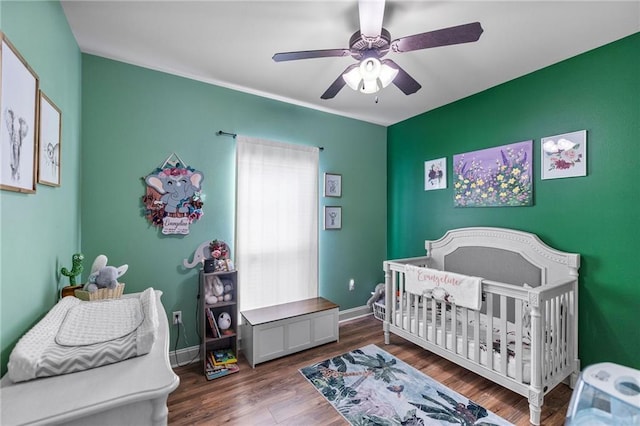 bedroom with a crib, wood finished floors, baseboards, and ceiling fan