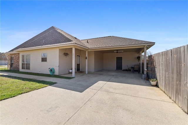 view of front of home with an attached carport, concrete driveway, roof with shingles, and fence