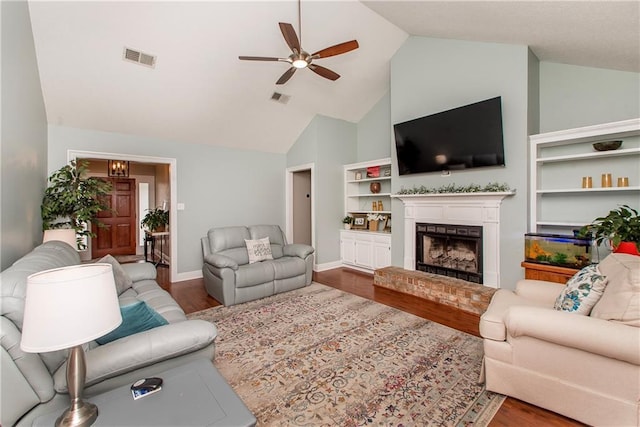 living room with ceiling fan, visible vents, a brick fireplace, and wood finished floors