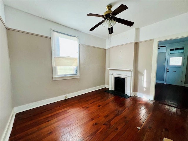 unfurnished living room with ceiling fan, baseboards, wood-type flooring, and a fireplace with raised hearth