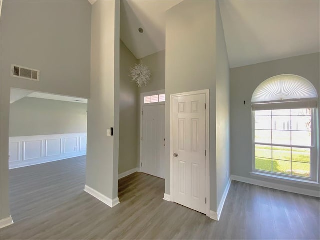 entrance foyer featuring baseboards, wood finished floors, visible vents, and high vaulted ceiling