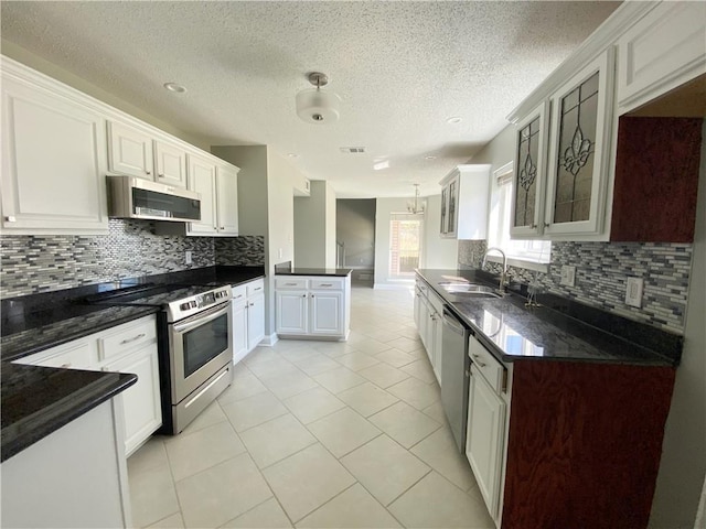 kitchen with glass insert cabinets, light tile patterned floors, decorative backsplash, stainless steel appliances, and a sink