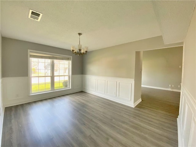 spare room featuring a notable chandelier, wainscoting, a textured ceiling, and wood finished floors