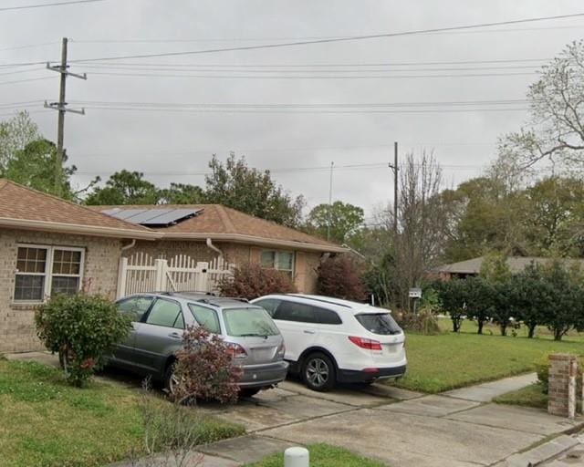 view of front of home featuring solar panels, a front lawn, fence, and brick siding