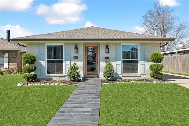 bungalow-style home featuring brick siding, a shingled roof, a front lawn, and fence