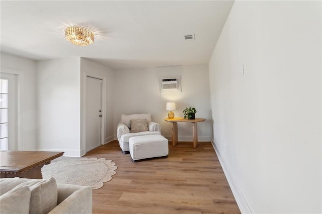 sitting room with light wood-type flooring, visible vents, baseboards, and a wall mounted air conditioner