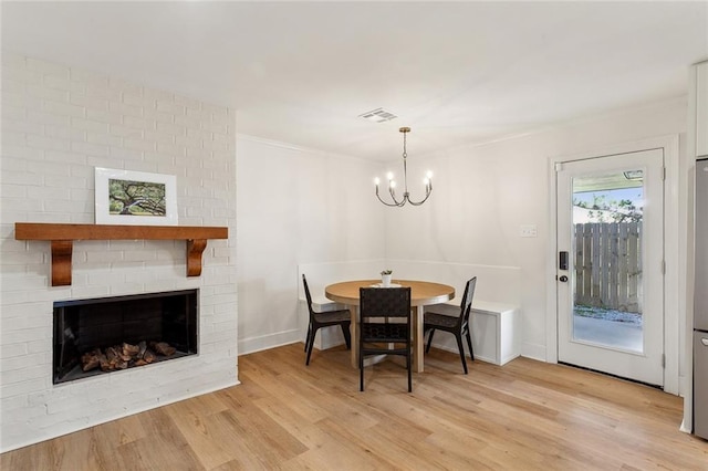 dining room featuring visible vents, a brick fireplace, baseboards, a chandelier, and light wood-type flooring