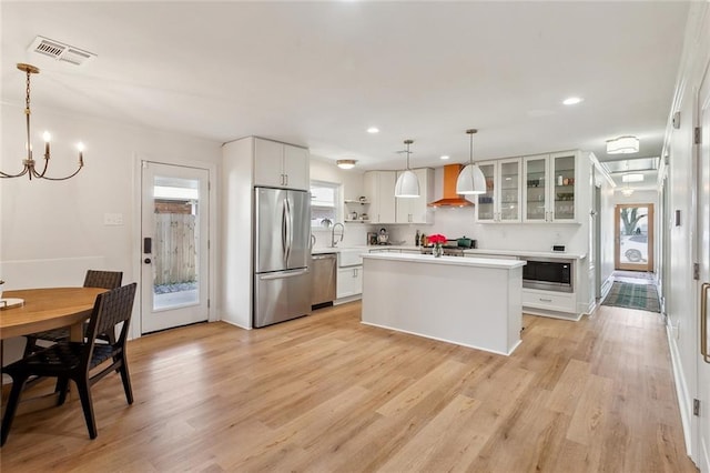 kitchen featuring light wood-type flooring, visible vents, stainless steel appliances, wall chimney exhaust hood, and light countertops