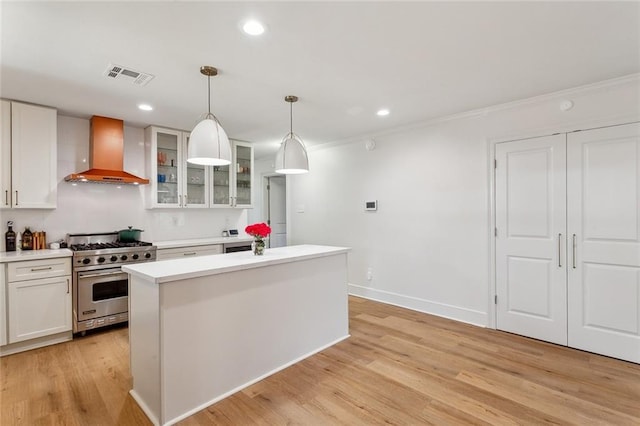 kitchen with white cabinetry, wall chimney range hood, visible vents, and premium range