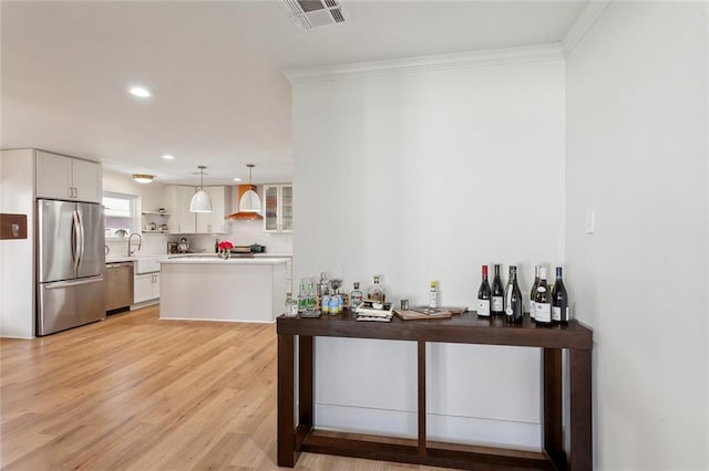 bar with visible vents, stainless steel appliances, light wood-style floors, wall chimney exhaust hood, and crown molding