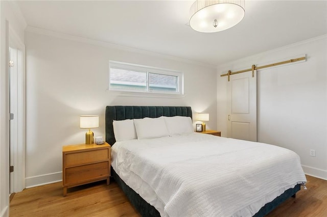 bedroom with baseboards, crown molding, a barn door, and wood finished floors