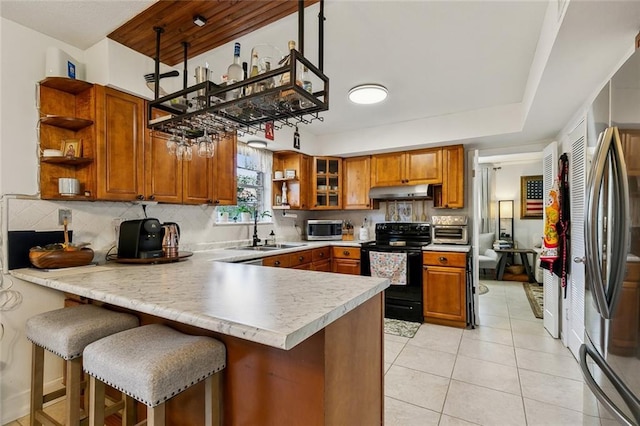 kitchen with open shelves, under cabinet range hood, appliances with stainless steel finishes, a peninsula, and a sink