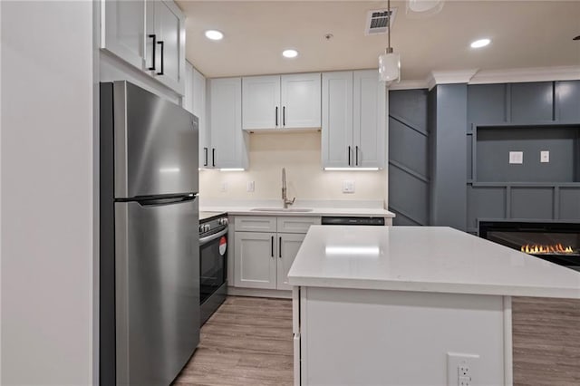 kitchen with visible vents, a center island, a glass covered fireplace, stainless steel appliances, and a sink