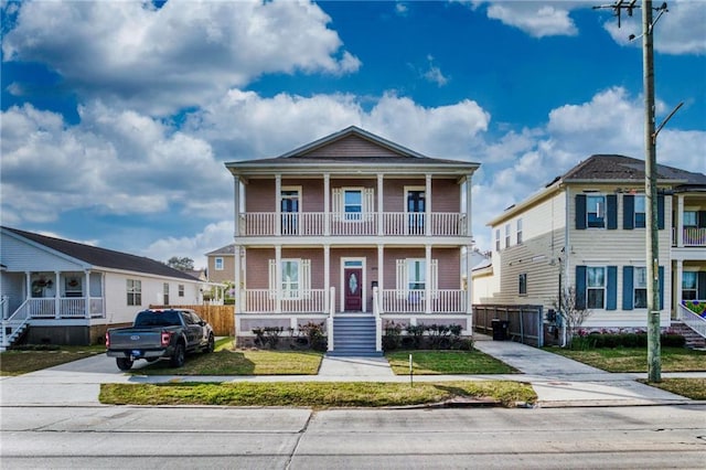 view of front of house featuring a balcony, covered porch, concrete driveway, and a front yard