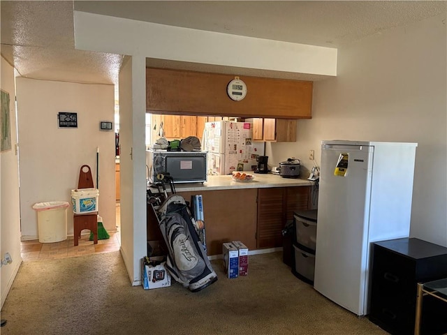 kitchen with brown cabinetry, freestanding refrigerator, and light carpet