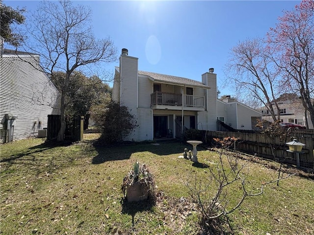 rear view of house featuring a yard, a balcony, a chimney, and fence