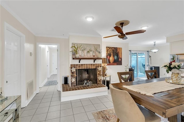 dining area with visible vents, a brick fireplace, ceiling fan, ornamental molding, and light tile patterned floors