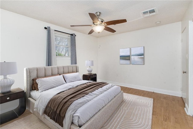 bedroom with visible vents, a ceiling fan, a textured ceiling, light wood finished floors, and baseboards