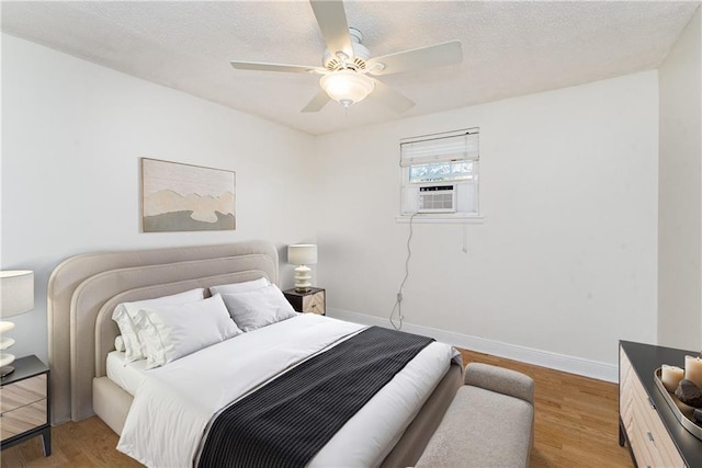 bedroom with ceiling fan, baseboards, cooling unit, wood finished floors, and a textured ceiling