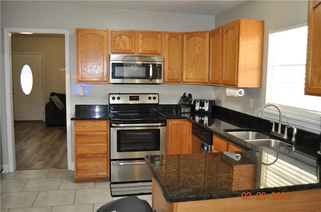 kitchen featuring a sink, appliances with stainless steel finishes, light tile patterned flooring, and dark stone countertops