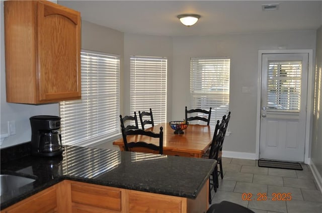 kitchen with visible vents, dark stone countertops, a peninsula, light tile patterned floors, and baseboards