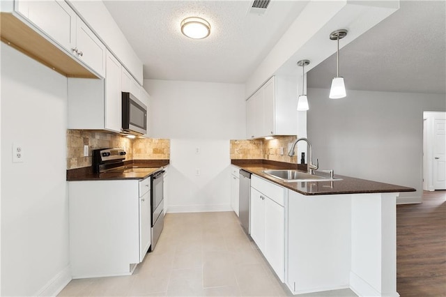 kitchen featuring dark countertops, a peninsula, stainless steel appliances, and a sink