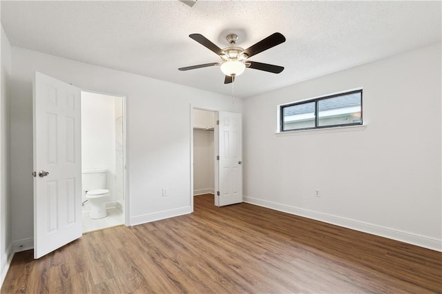 unfurnished bedroom with wood finished floors, baseboards, ensuite bath, a textured ceiling, and a walk in closet