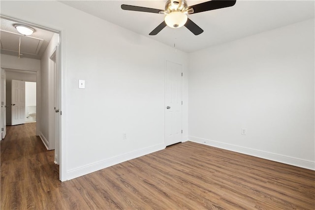 empty room with attic access, wood finished floors, baseboards, and ceiling fan