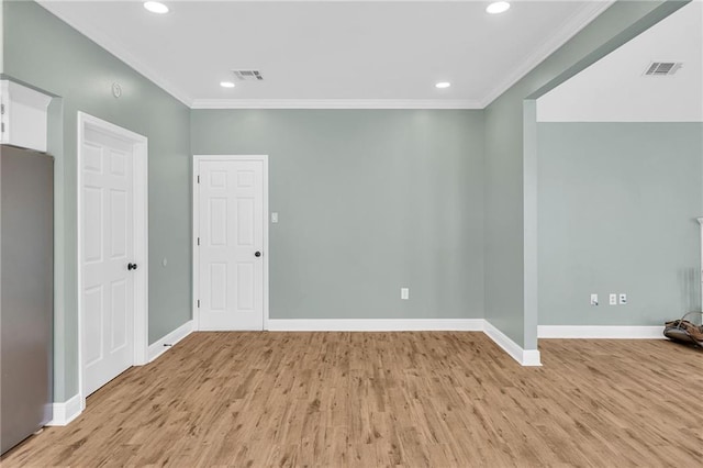 spare room with light wood-type flooring, baseboards, visible vents, and ornamental molding