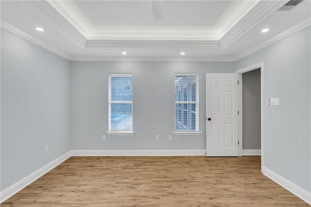 unfurnished room featuring a tray ceiling, light wood-style flooring, baseboards, and visible vents