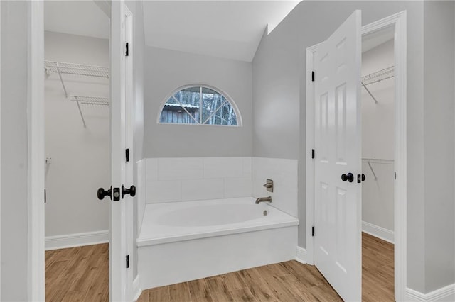 bathroom with a spacious closet, baseboards, a garden tub, and wood finished floors