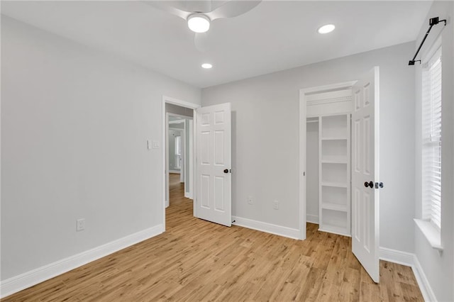 unfurnished bedroom with multiple windows, baseboards, a walk in closet, and light wood finished floors