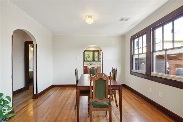 dining area with visible vents, light wood-style flooring, arched walkways, crown molding, and baseboards