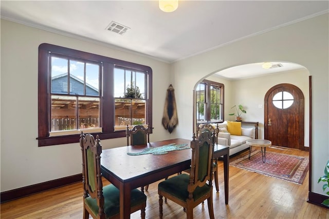 dining area featuring light wood-type flooring, visible vents, ornamental molding, arched walkways, and baseboards