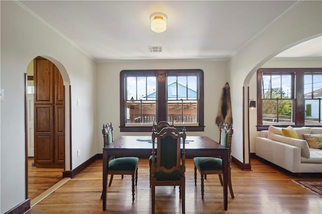 dining area featuring arched walkways, visible vents, a healthy amount of sunlight, and wood finished floors