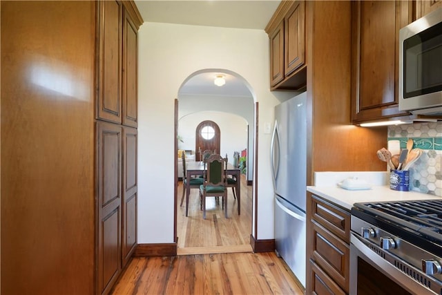 kitchen with arched walkways, decorative backsplash, light countertops, appliances with stainless steel finishes, and light wood-type flooring