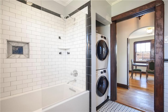 laundry area featuring baseboards, stacked washing maching and dryer, laundry area, light wood-style flooring, and crown molding