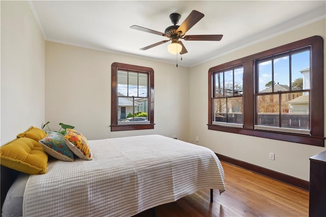 bedroom with multiple windows, crown molding, baseboards, and wood finished floors