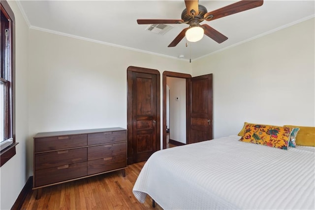 bedroom featuring crown molding, wood finished floors, visible vents, and ceiling fan