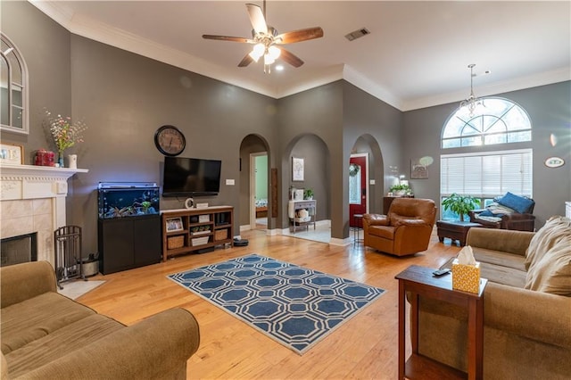 living area featuring visible vents, crown molding, a tiled fireplace, wood finished floors, and arched walkways