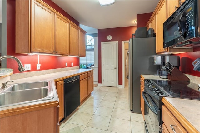 kitchen with brown cabinetry, light tile patterned flooring, a sink, black appliances, and light countertops