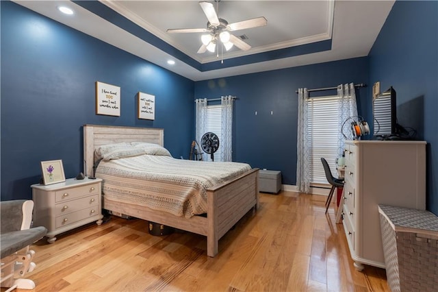 bedroom featuring light wood-style flooring, a raised ceiling, a ceiling fan, and ornamental molding