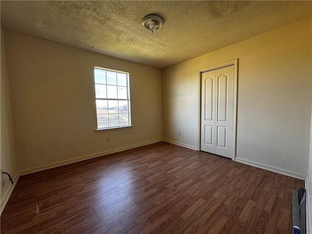 spare room with a textured ceiling, dark wood-type flooring, and baseboards