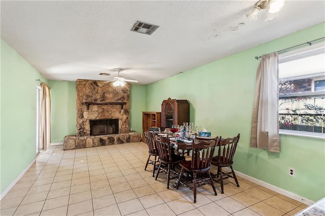 tiled dining room featuring visible vents, a ceiling fan, a fireplace, and a textured ceiling