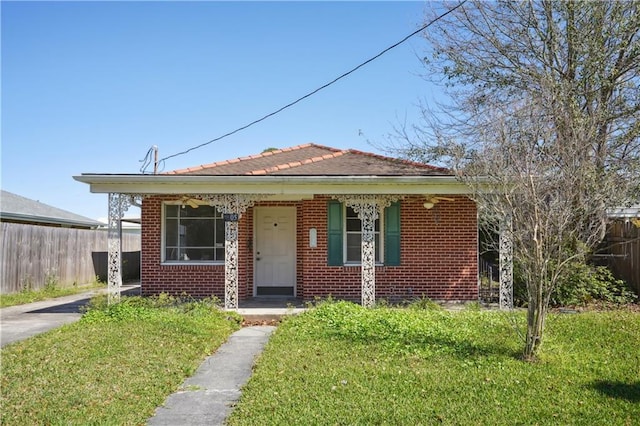 bungalow-style house with brick siding, a tile roof, a front lawn, and fence