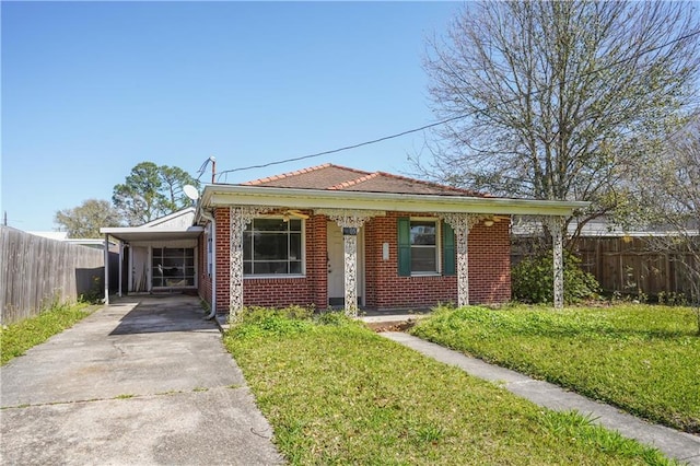 bungalow featuring brick siding, an attached carport, a front lawn, fence, and driveway