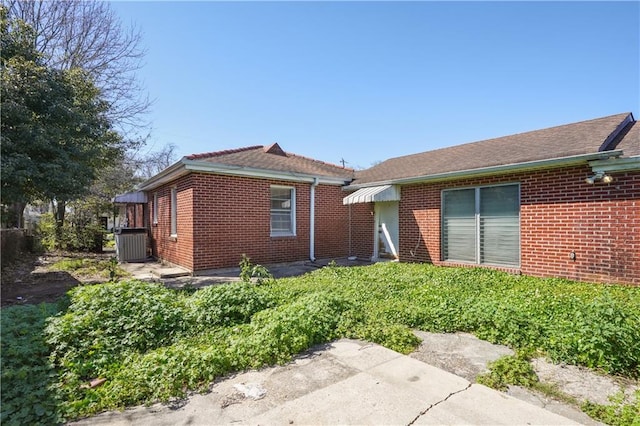 back of property featuring brick siding and central AC