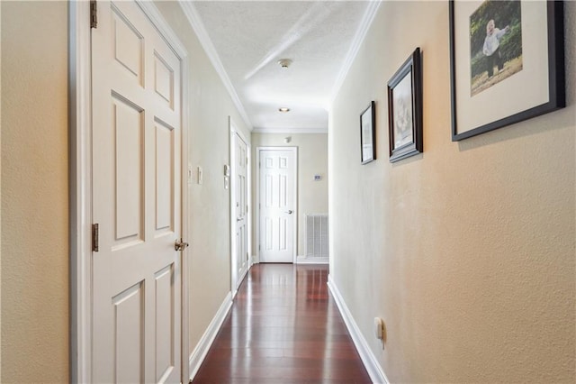 corridor featuring dark wood-style floors, visible vents, baseboards, crown molding, and a textured wall